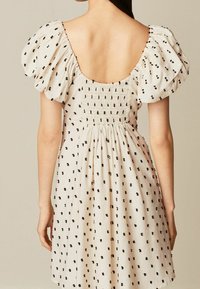 Vestido de algodón con mangas abullonadas, base crema, patrón de lunares negros y espalda fruncida. Escote profundo que revela la espalda. Diseño de falda fluida.