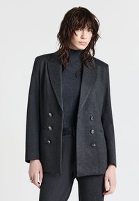 Blazer doppiopetto grigio scuro in tessuto morbido. Caratterizzato da ampi rever, sei bottoni lucidi e una vestibilità rilassata, abbinato a un top scuro a coste.