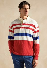 Pika pikahemeliku särk on varrukateta ja sellel on horisontaalsed punased, valged ja sinised triibud, beež kaelus ning rinnal on väike tikand.