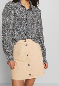 Floral button-up blouse in black, featuring multicolored tiny flowers. Paired with a beige denim skirt, button-front design, and two pockets.