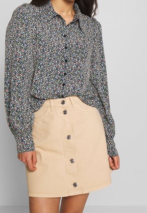 Blusa a maniche lunghe con bottoni in nero, caratterizzata da piccoli fiori multicolori. Accostata a una gonna in denim beige, con chiusura a bottoni sul davanti e due tasche.