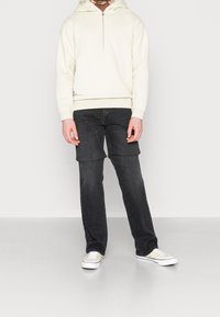 Sudadera con capucha de color blanco roto con cremallera, combinada con pantalones cargo gris oscuro con bolsillos laterales. Zapatillas blancas completan el conjunto.