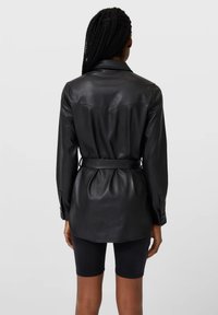 Chemise en cuir noir avec un col, taille ceinturée et manches longues. Comprend un empiècement au dos et des plis pour plus de détails.