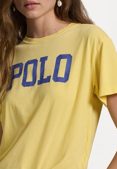 Geltona medvilninė marškinė su mėlynu "POLO" grafinu priekyje. Trumpomis rankovėmis ir apvaliu iškirpimu, su laisvu siluetu.