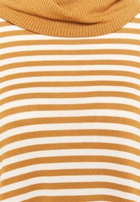 Gros plan sur un vêtement à rayures horizontales moutarde et blanches avec un col roulé côtelé de couleur moutarde.