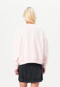 Pink sweatshirt with a relaxed fit, crew neckline, and ribbed cuffs. Paired with a dark denim skirt featuring pockets. Smooth texture.