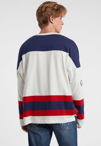 Langarmshirt in Creme mit navyblauen und roten horizontalen Streifen. Weicher Stoff mit lockerer Passform und gespaltenem Saumdetails.