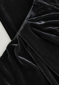 Tela de terciopelo negro con una textura suave, que presenta pliegues suaves y un ligero brillo. El material tiene un aspecto rico y lujoso.