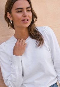 Witte sweatshirt met ronde hals, geribbelde manchetten en pofmouwen. Glad textuur met een casual pasvorm, gecombineerd met oorringen.