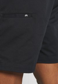 Černé bavlněné krátké kalhoty s hladkou texturou, na boční kapse je malý bílý logo Nike SB a zakončené jsou čistým lemem.