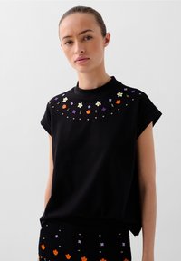 Czarny bawełniany t-shirt z krótkimi, podwijanymi rękawami, z kolorowymi, kwiatowymi haftami w okolicy dekoltu. Miękka tekstura.