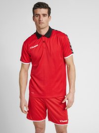 Röd sportpolo med svart krage, logotyp på bröstet och vita detaljer. Matchas med röda shorts av lätt material.