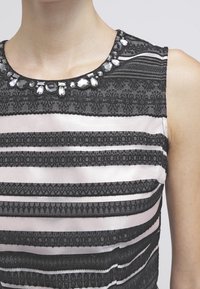 Svart och ljusrosa ärmlös klänning med horisontella ränder, strukturerade mönster och en dekorativ halsringning med pärlaccenter.