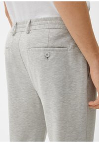 Lichtgrijze joggers met een soepele textuur, een elastische tailleband en twee achterzakken met knoopsluitingen.