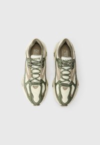 Tênis Lacoste com um cabedal de materiais mistos nas tonalidades verde, bege e creme, com sobreposições intrincadas e detalhes texturizados.