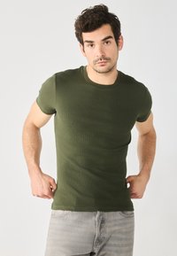 Camiseta de rayas verde oliva con mangas cortas, escote redondo, diseño ajustado, combinada con jeans de mezclilla gris claro.