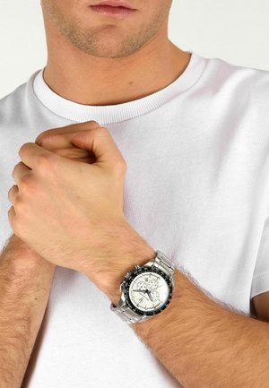 Uomo con camicia bianca che unisce le mani, mostrando un orologio da polso in metallo argento con quadrante bianco e ghiera nera al polso sinistro.
