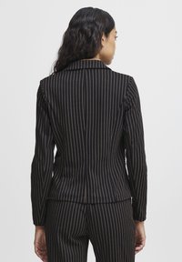 Black pinstriped blazer with brown vertical lines, tailored fit, notch lapels, and long sleeves. Features a smooth, textured fabric.