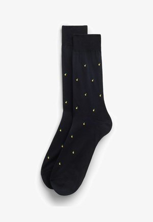 Een paar zwarte enkelsokken met kleine gele ananaspatronen die gelijkmatig over de stof verdeeld zijn.