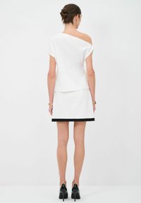 Top bianco senza spalle con maniche corte, abbinato a una gonna bianca con orlo nero. Tessuto liscio, design minimalista. Tacchi neri.