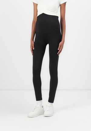 Sorte høyt liv leggings laget av elastisk stoff, med en glatt tekstur og tettsittende design. Kombinert med hvite joggesko.