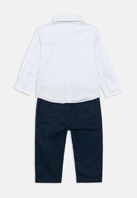 Svetlomodrá a biela pruhovaná košeľa s dlhými rukávmi a gombíkovým golierom, skombinovaná s tmavomodrými nohavicami s dvoma zadnými vreckami.