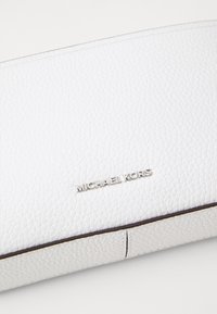 Valge nahast rahakott, millel on krobeline tekstuur, esiküljel hõbedane "MICHAEL KORS" logo foonitud ja siledad tumedad servad.