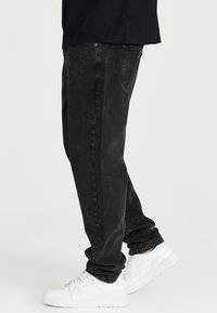 Jeans de mezclilla negra con corte recto, que cuentan con bolsillos traseros y un ligero desgastado. Combinados con zapatillas blancas.
