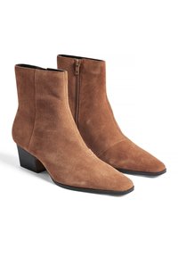 Bottines en daim marron avec un bout pointu, un talon bloc de hauteur intermédiaire et des détails de zip sur le côté. Texture lisse avec des accents minimaux.