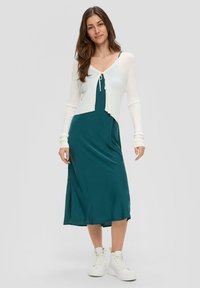 Turkusowa sukienka midi z białym, krótkim kardiganem z prążkowanej dzianiny, związywanym z przodu, z długimi rękawami i bocznym rozcięciem. Połączona z białymi platformowymi sneakersami.