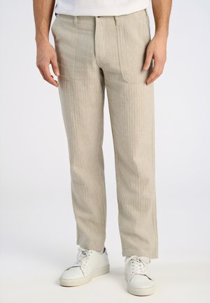 Pantalones a rayas beige con corte recto, con cremallera y dos bolsillos frontales; combinados con zapatillas blancas.