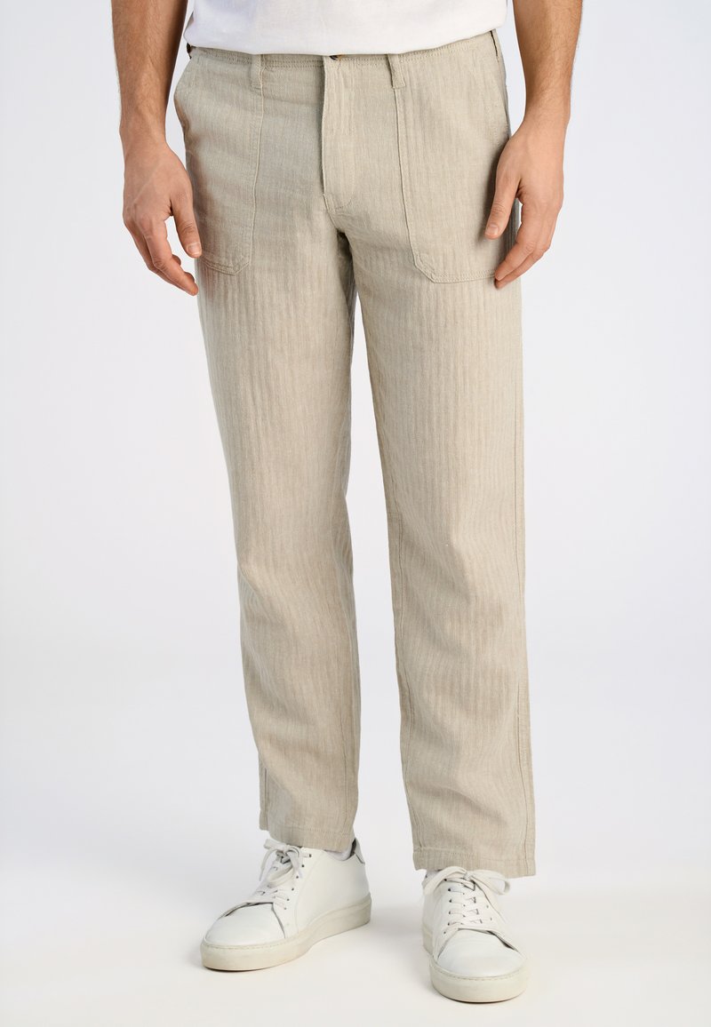 Beige gestreepte broeken met een rechte fit, voorzien van een ritssluiting en twee voorkruiszakken; gecombineerd met witte sneakers.