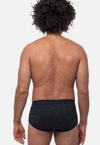 Schwarz gestreifte Unterhosen mit glatter Textur und elastischem Bund, von hinten gesehen, an einer Person mit lockigem Haar und nackter Haut.