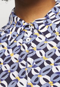 Mönstrad blus med krage, tillverkad av lättviktig tyg med en geometrisk design i blått, vitt och gult.