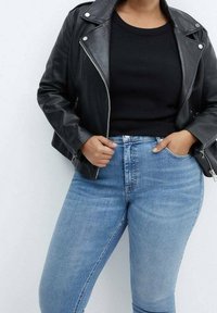 Personne portant une veste en cuir noire sur un haut noir et un jean taille haute bleu clair, une main dans la poche et l'autre tenant la veste.