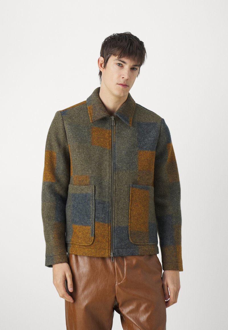 Wool blend jacket featuring a zip closure, pointed collar, and patchwork design in green, blue, and orange with two front pockets.