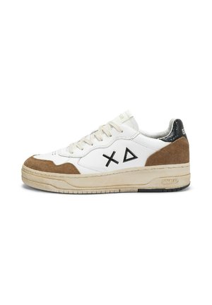 Baskets blanches avec des patches en suède marron, un accent noir au talon, des symboles "X" et triangle noirs sur le côté, et une semelle beige avec un relief visible.