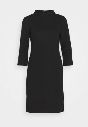 Robe noire texturée longueur genou avec manches trois-quarts et petit col montant, détail fente au dos.
