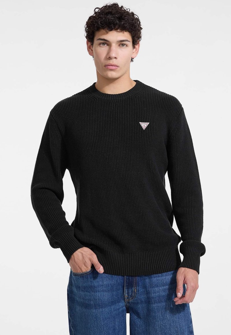 Schwarzer gerippter Strickpullover mit rundem Halsausschnitt und einem kleinen Marken-Dreieck-Patch. Verfügt über lange Ärmel und eine strukturierte Oberfläche.