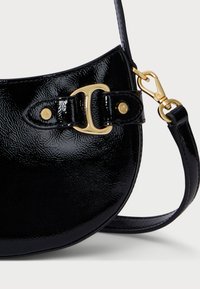 Fekete lakk bőr, ívelt formájú keresztbody táska arany színű fém díszítésekkel és oldalsó záró mechanizmussal. Állítható pántot tartalmaz.