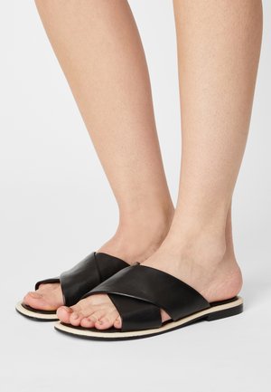 Sandales en cuir noir avec des bretelles croisées, design plat et semelle de couleur claire. orteils découverts, texture lisse, détails minimalistes.