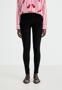 Leggings noirs ajustés en matériau doux et texturé, associés à un shirt rayé rouge ornés de broderies florales et des chaussures à imprimé léopard.