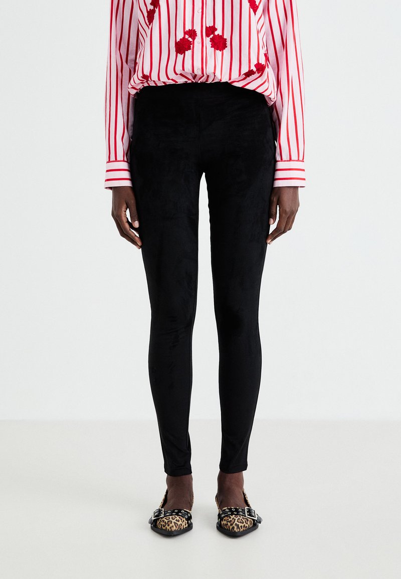 Leggings noirs ajustés en matériau doux et texturé, associés à un shirt rayé rouge ornés de broderies florales et des chaussures à imprimé léopard.