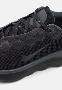 Gros plan d'une chaussure de course Nike noire avec tissu en mesh, lacets à motifs et semelle ondulée.
