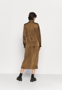 Długa, brązowa satynowa sukienka z kołnierzykiem i długimi rękawami, charakteryzująca się gładką fakturą, sięgająca tuż poniżej kolan, zestawiona z czarnym obuwiem.