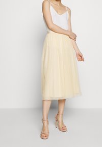 Jupe midi en tulle jaune clair avec des pois texturés, associée à un top à bretelles spaghetti blanc et des sandales à talons nus.