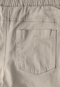 Ljusbeige tyg med en texturerad yta, med resårmidja och en enda bakficka med stickningsdetalj.