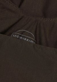 Bruin stof met een textuur op het oppervlak en een label met "intimissimi" in lichtgrijs, geplaatst nabij een geplooide naad.
