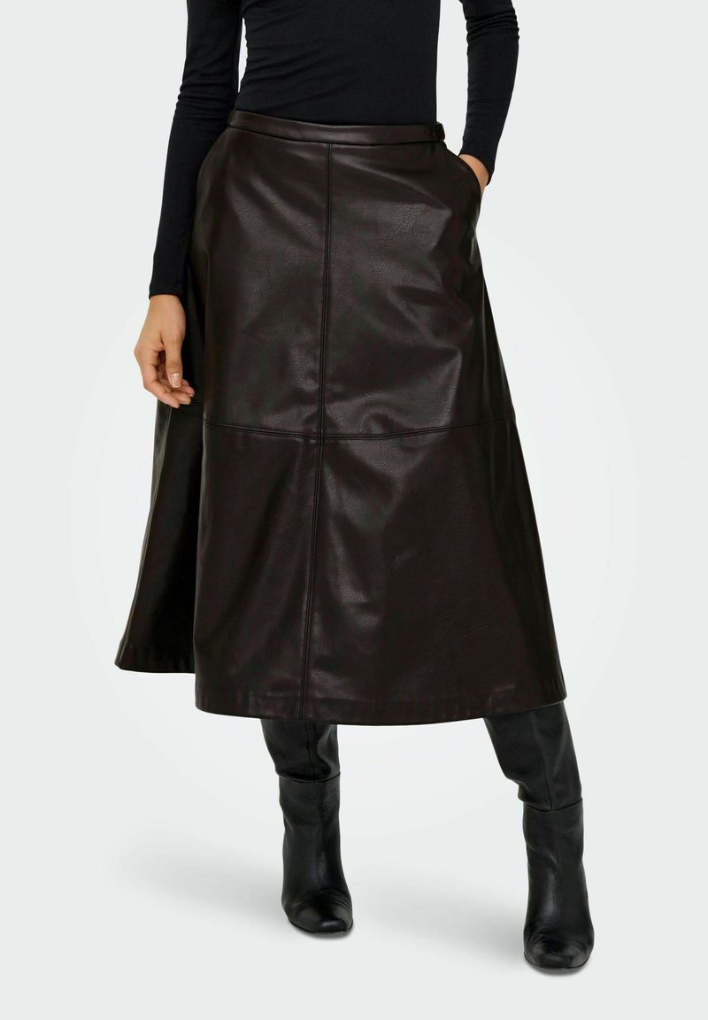 Jupe midi en cuir marron avec une silhouette évasée, présentant des détails de coutures et une texture lisse et brillante. Associée à des bottes noires jusqu'aux genoux.