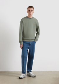 Lichtgroene sweatshirt met een ronde halslijn en geribbelde manchetten, gecombineerd met blauwe spijkerbroek en grijze hardloopschoenen. Eenvoudig ontwerp, casual pasvorm.